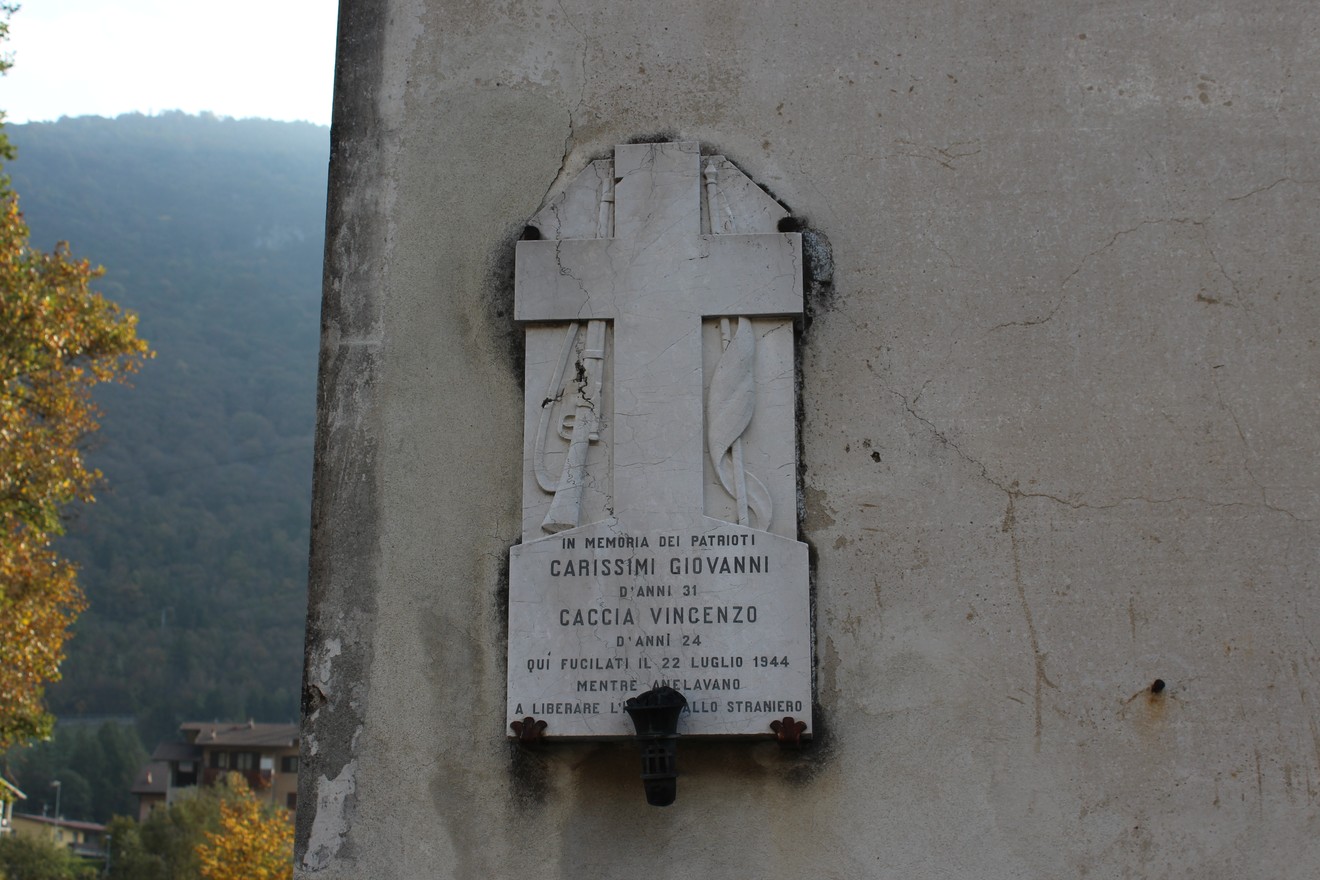 Lapide commemorativa dedicata a Caccia e Carissimi, posta su una parete con sfondo naturale.