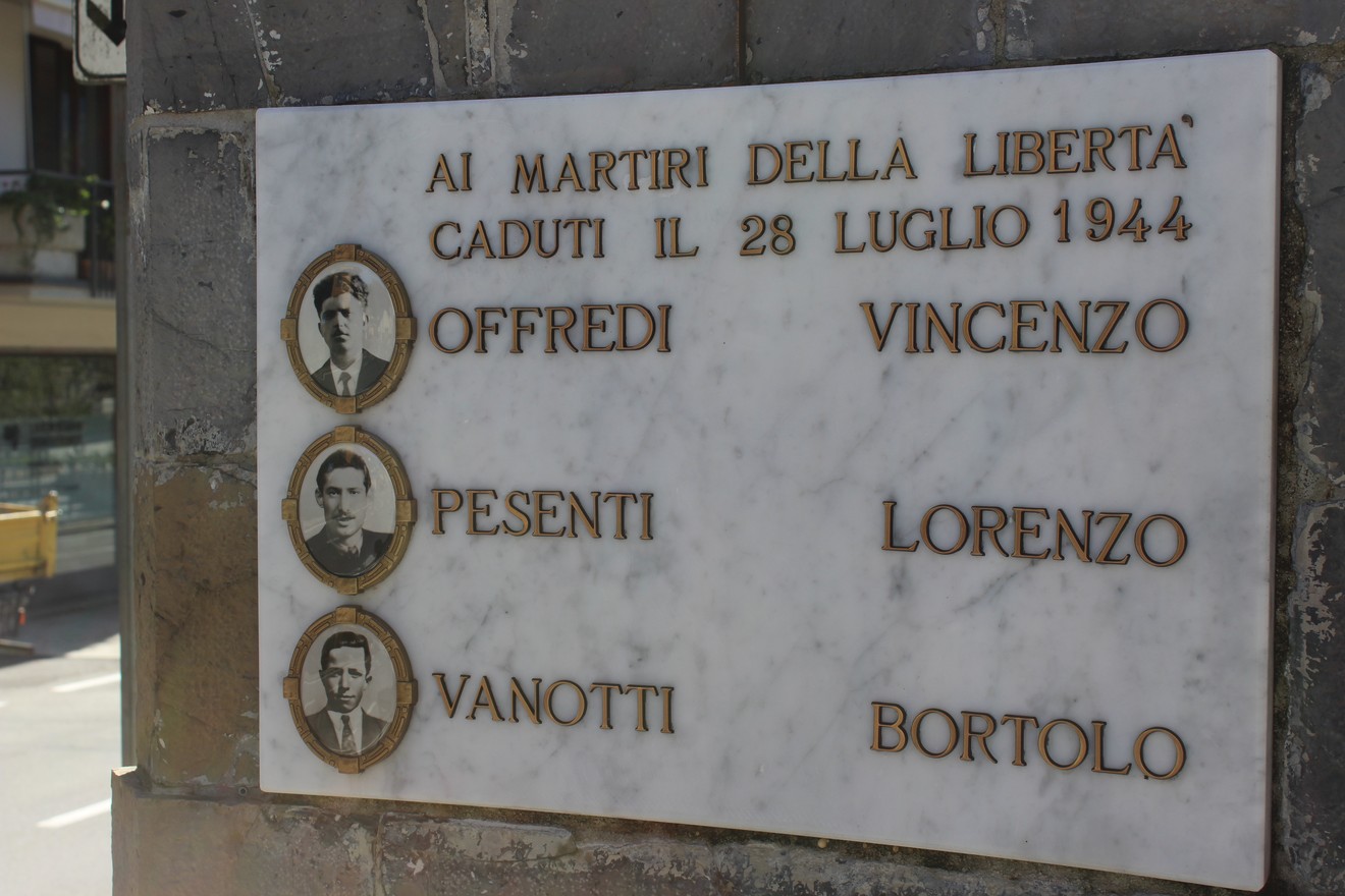 Cippo commemorativo in marmo dedicato ai martiri della libertà a Offredi, Pesenti e Vanotti, con ritratti.