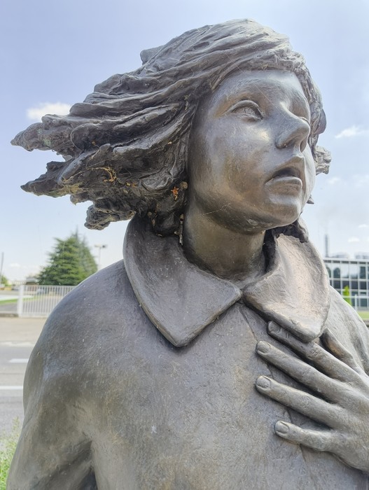 Scultura di bronzo che ritrae una giovane ragazza con i capelli al vento, esprimendo emozione e dignità.