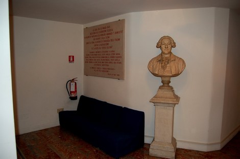 Lapide commemorativa con busto e divano in un ambiente interno, richiamando la "beffa del Teatro Goldoni".