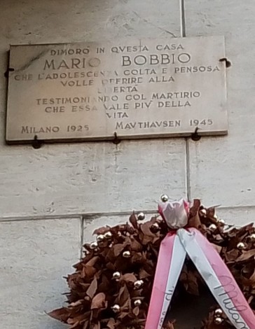 Lapide commemorativa di Mario Bobbio, situata a Milano, adornata con una corona di fiori.