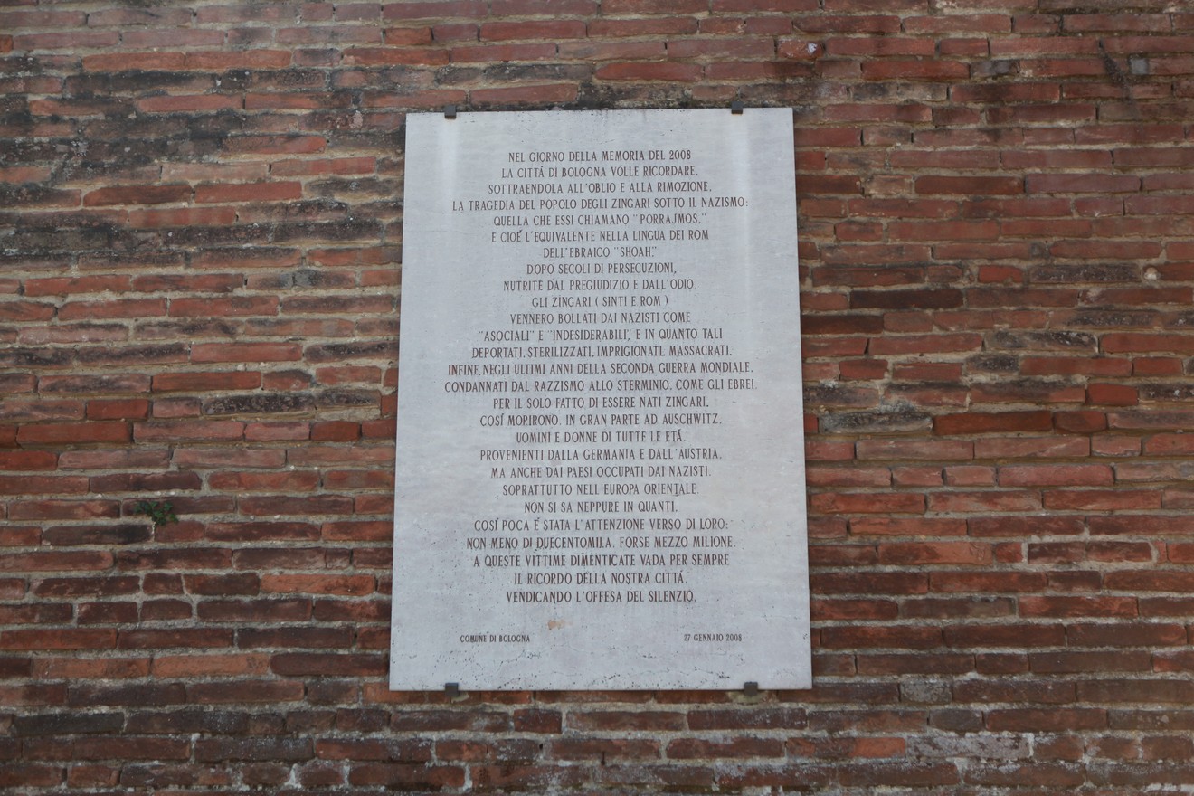 Lapide commemorativa dedicata alle vittime del Porrajmos, collocata su un muro di mattoni.