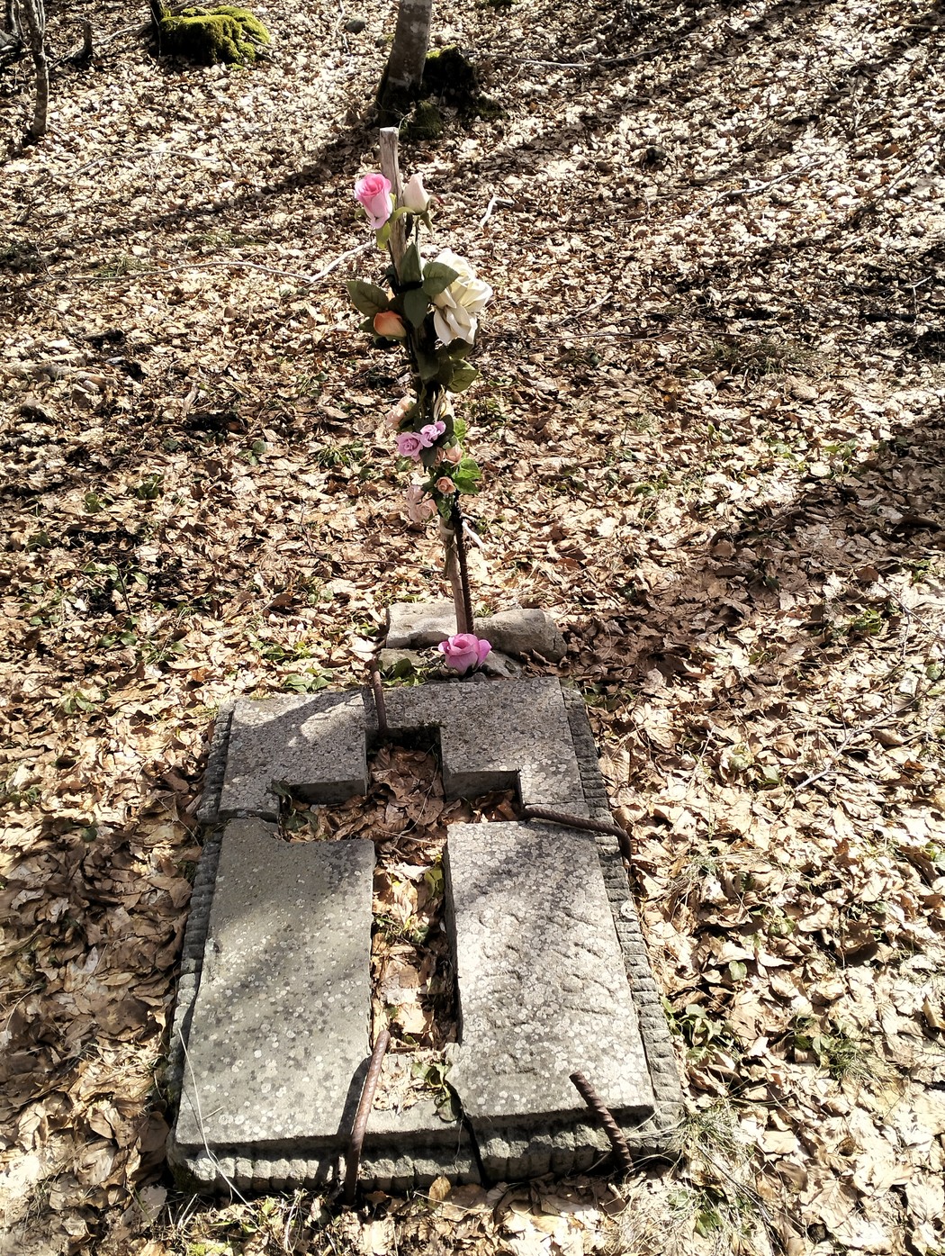 Cippo commemorativo avvolto da foglie secche e decorato con fiori, simbolo di memoria e rispetto.