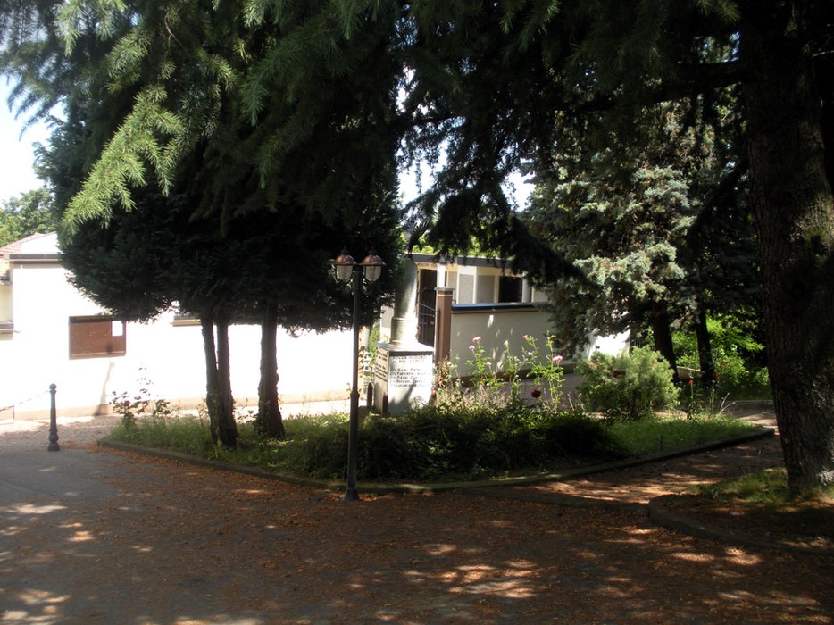 Cippo commemorativo dedicato ai caduti, circondato da alberi e vegetazione a Rocca de' Giorgi.
