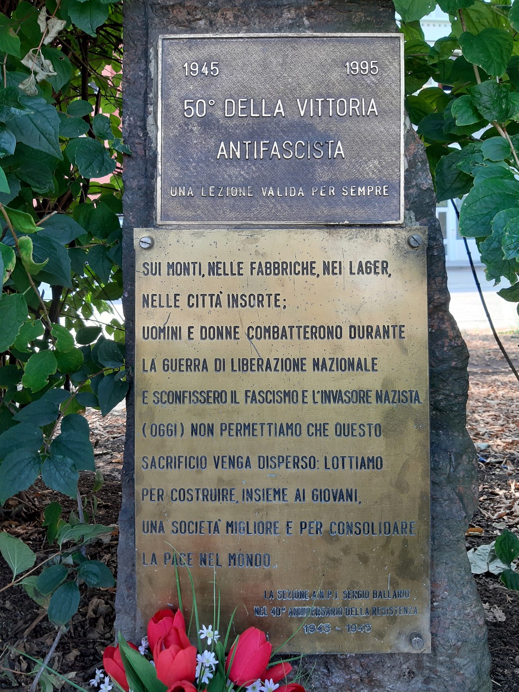 Cippo commemorativo per il 40° e 50° anniversario della Resistenza, con decorazioni floreali e rilievi storici.