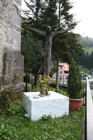 Busto commemorativo a Don Menguzzo, con raffigurazione artistica e lapide in un contesto naturale.