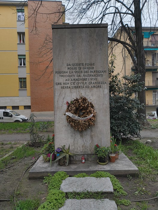 Monumento commemorativo ai partigiani uccisi a San Ruffillo, ricco di piante e un omaggio floreale.
