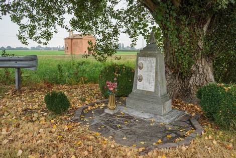 Cippo commemorativo a Rustichello e Lodi, immerso nella natura con un campo sullo sfondo.
