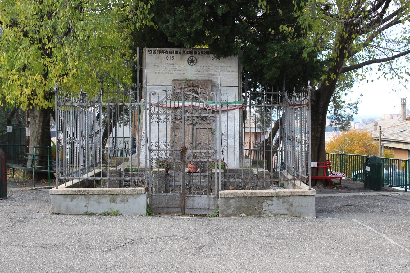 Monumento ai caduti di Quezzi circondato da una ringhiera, immerso in un ambiente tranquillo e alberato.