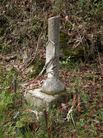Cippo commemorativo dedicato a Giuseppe Mazzini, circondato da vegetazione e catene, in un contesto naturale.