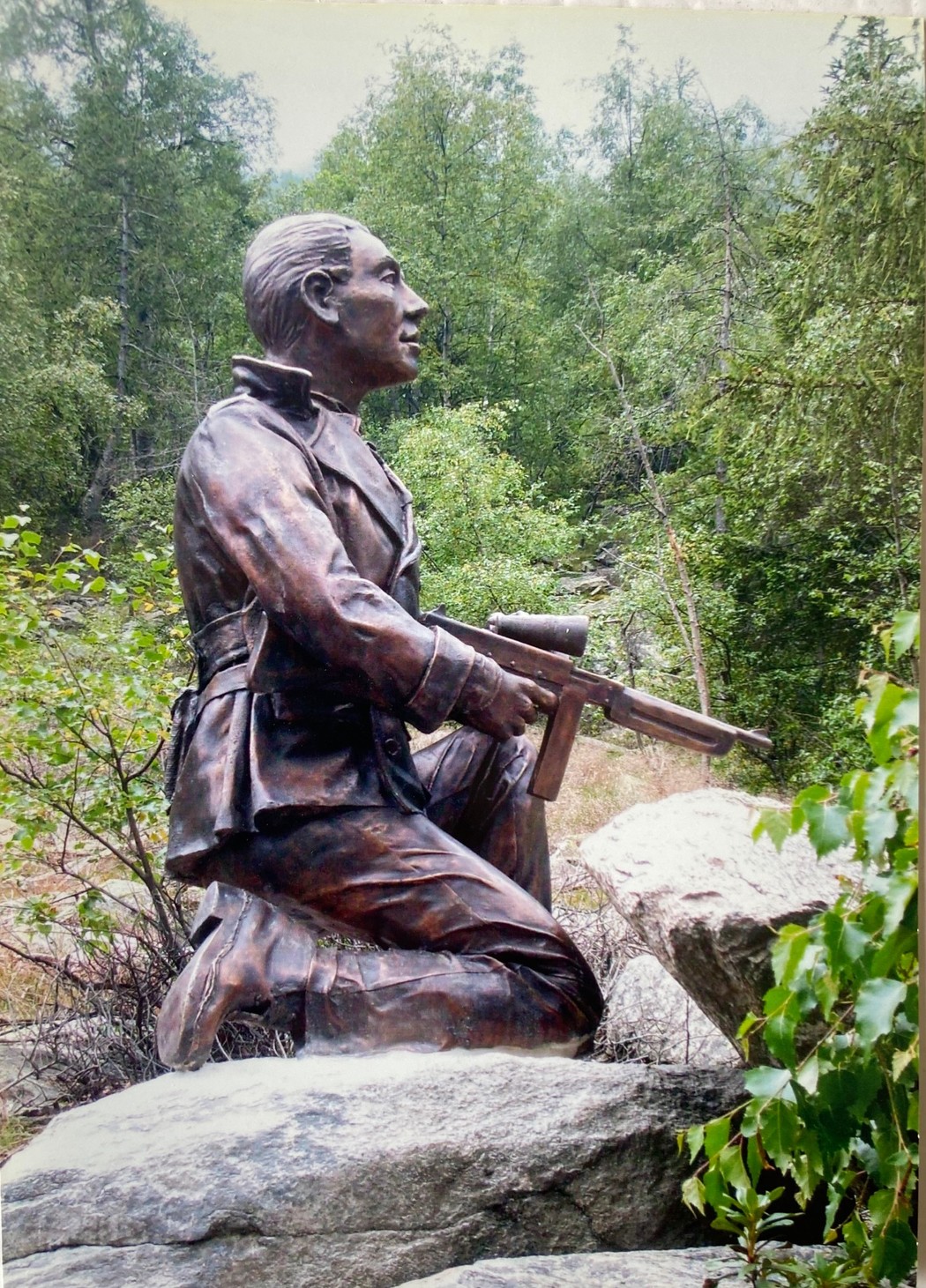 Monumento a Ilardi, statua bronzea di un soldato inginocchiato tra la vegetazione e le rocce circostanti.