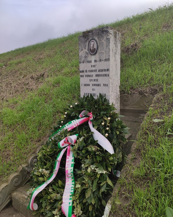 Cippo commemorativo di Bertoni con decorazioni floreali, situato su un pendio erboso.