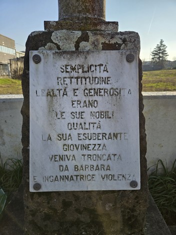 Cippo commemorativo a Guatelli con iscrizioni che celebrano valori di onestà e gioventù interrotta.