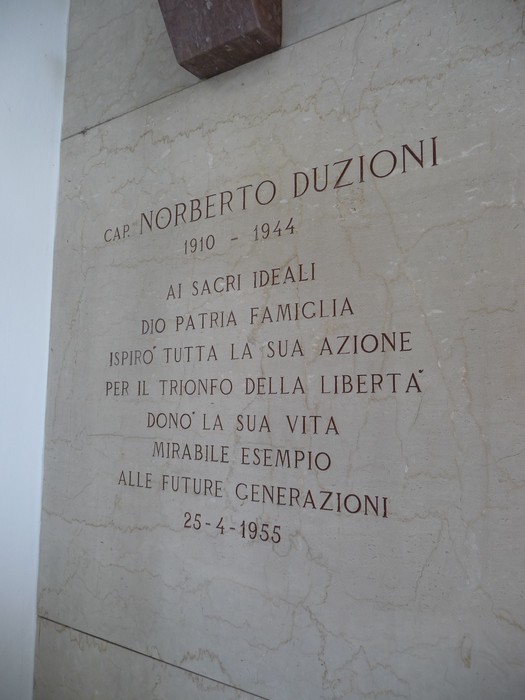Lapide commemorativa dedicata a Norberto Duzioni, con testo inciso su pietra che celebra il suo sacrificio.