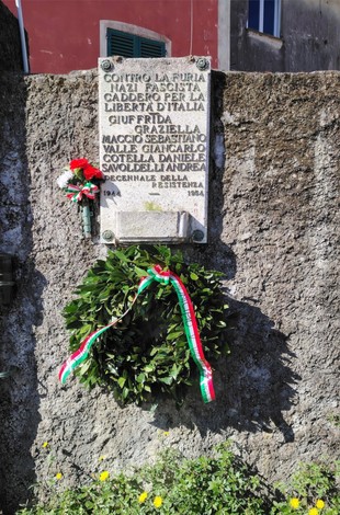 Lapide commemorativa ai Martiri di Rocca dei Corvi, con omaggio floreale e decorazioni tricolori.