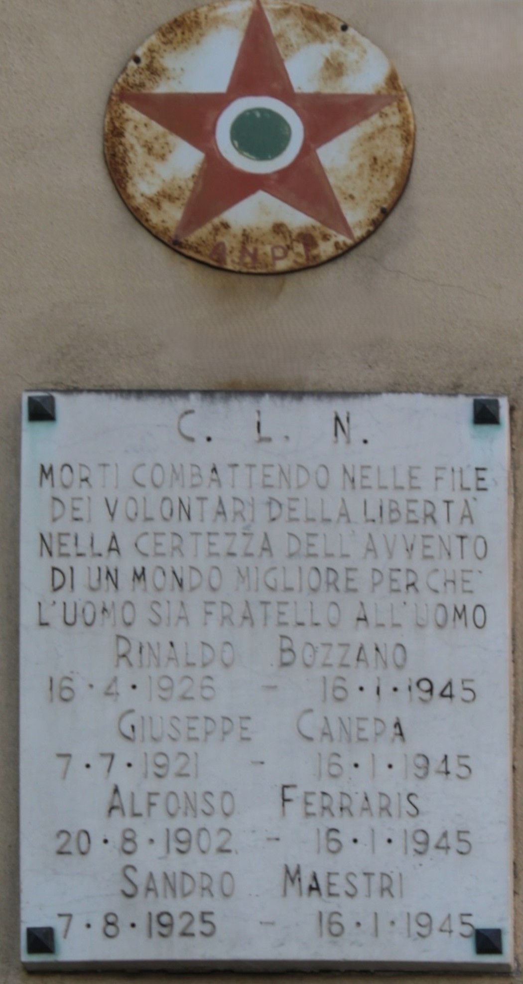Stella rossa a cinque punte con cerchio centrale sopra una lapide marmorea con iscrizione, su parete esterna.