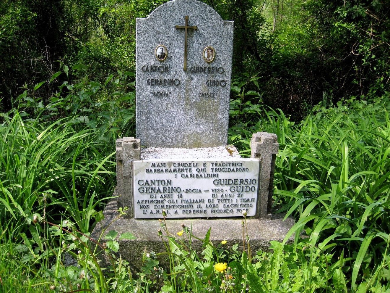 Cippo commemorativo dedicato a Canton e Guiderso, immerso nella vegetazione.