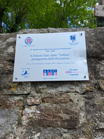 Targa commemorativa dedicata a Ernesto Taiti, protagonista della Resistenza, affissa su un muro in un contesto naturale.