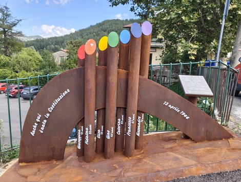 Monumento in metallo dedicato alle vittime della strage di Castagno, con elementi colorati e scritte commemorative.