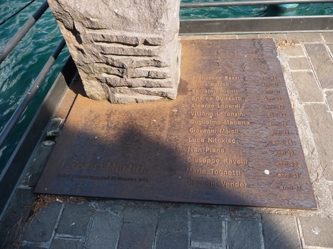 Stele commemorativa con i nomi dei Tredici Martiri, incisa su metallo, posizionata lungo un molo.