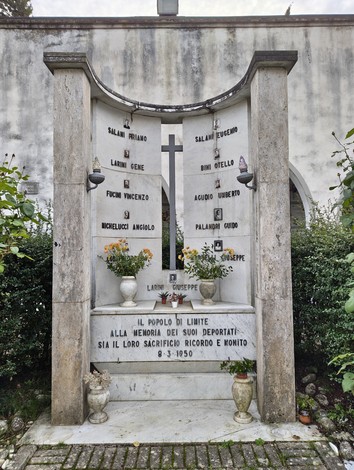 Monumento commemorativo dedicato ai deportati, con nomi incisi e decorazioni floreali. Atmosfera di riflessione e rispetto.