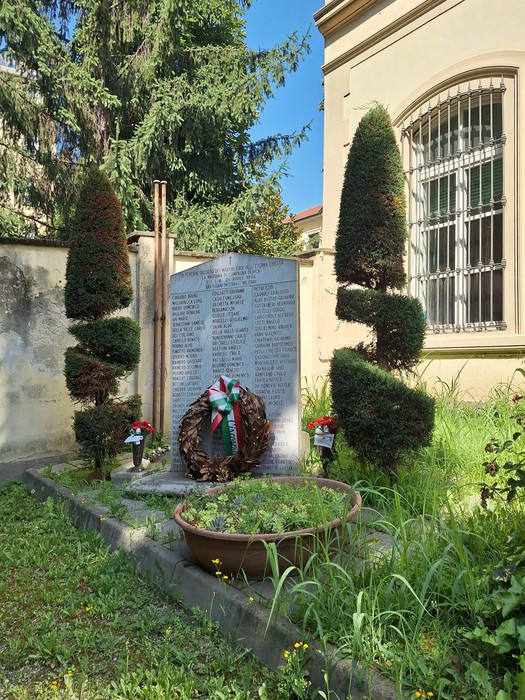 Monumento ai Martiri della Libertà di Madonna di Campagna, circondato da piante verdi e decorazioni floreali.