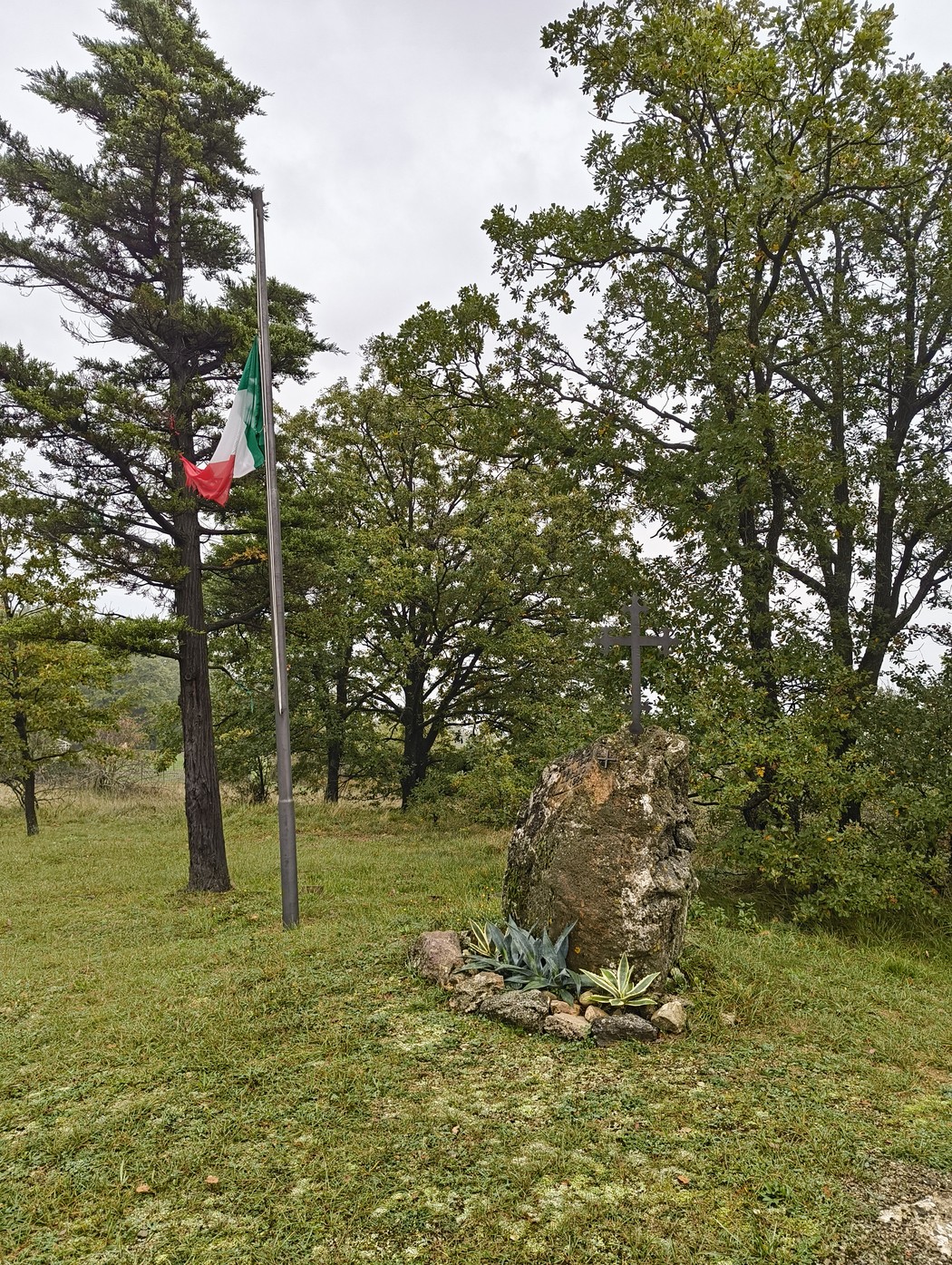Monumento commemorativo per l'eccidio di Pian di Setta, circondato da vegetazione e bandiera italiana.