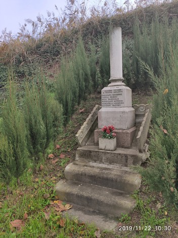 Cippo commemorativo a Ceconato con gradini e decorazioni, circondato da vegetazione.