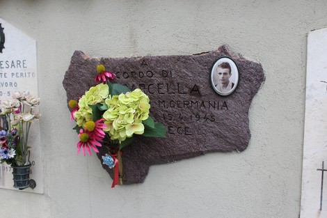 Lapide commemorativa di Barcella con fiori e ritratto, in memoria di una persona scomparsa nel 1945.