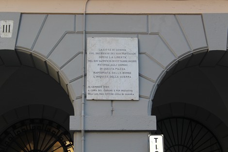 Lapide commemorativa che denuncia la guerra, collocata in una piazza con architettura storica.