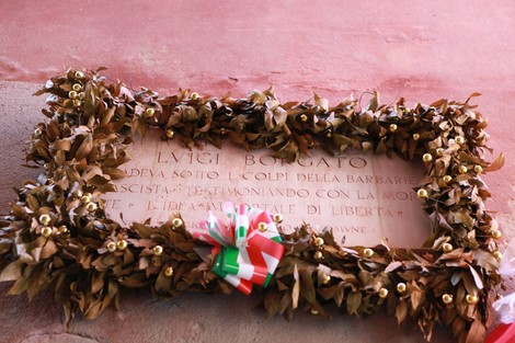 Lapide commemorativa decorata con una corona di foglie, posizionata su una parete.