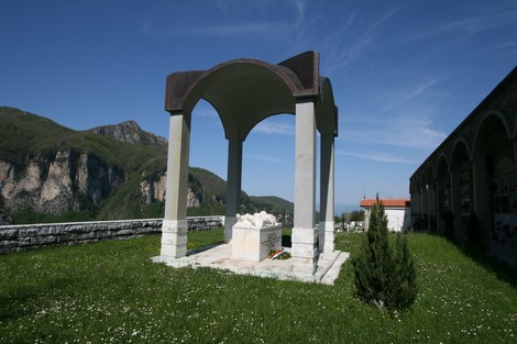 Monumento al cimitero di Vinca, immerso nel verde con vista sulle montagne circostanti.