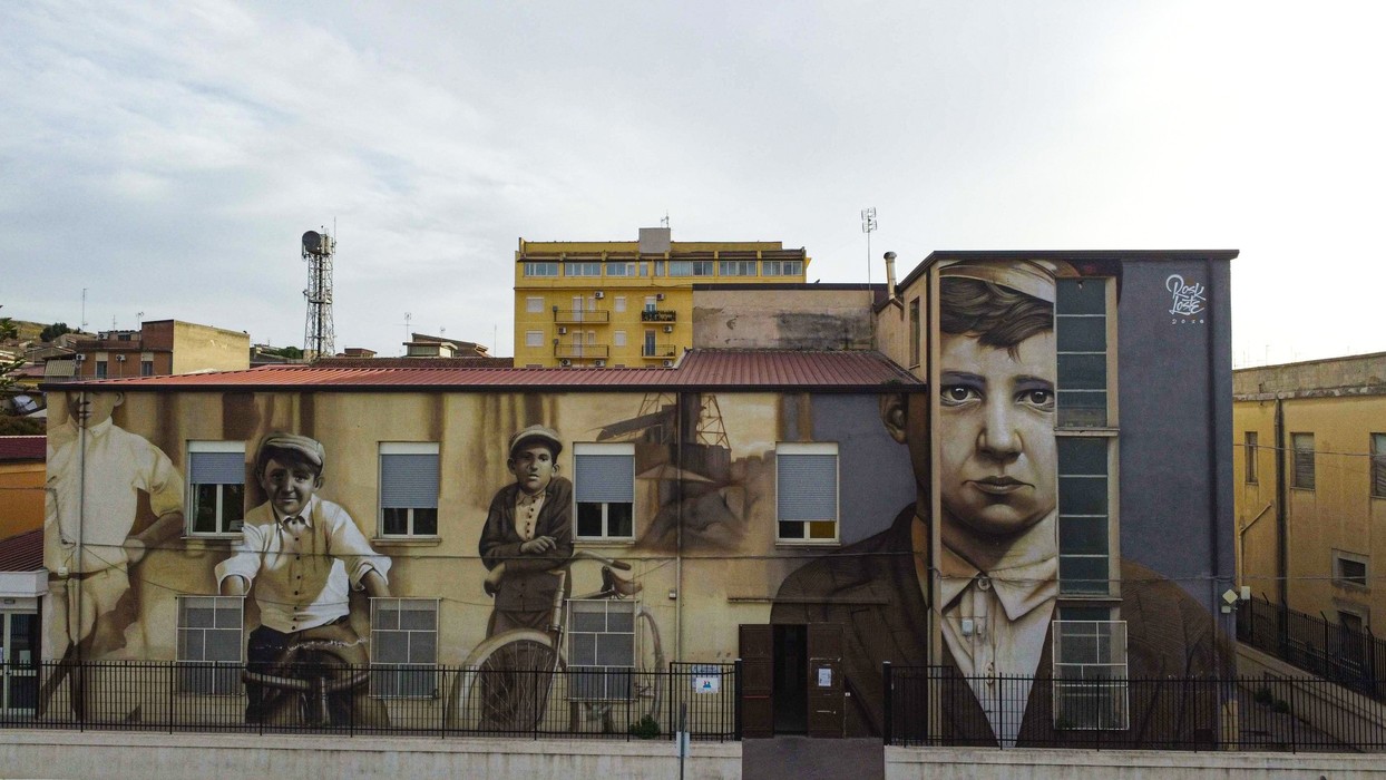 Murales artistici su un edificio a Butera, raffiguranti personaggi storici e locali in un'opera di street art.