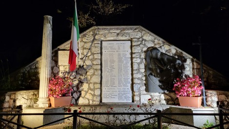Monumento ai caduti di Rocca Canterano, dedicato alla memoria dei soldati, illuminato di notte tra fiori e bandiere.