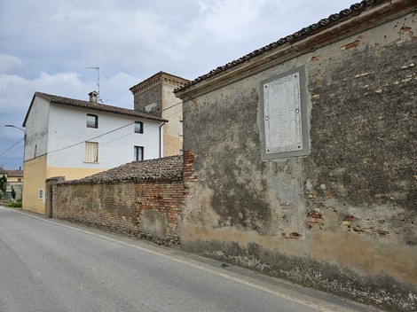 Lapide commemorativa murata su un edificio in una strada di Cavezzo, circondata da un paesaggio urbano.