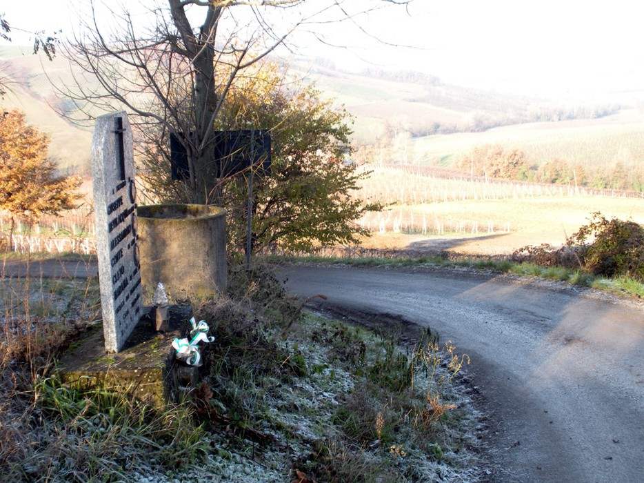 Cippo commemorativo a Bevilacqua, circondato da un paesaggio collinare. Atmosfera tranquilla e mistica.