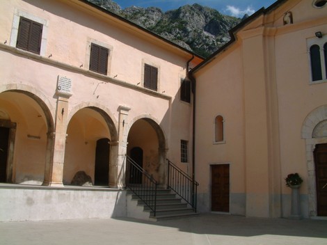 Lapide commemorativa dedicata a Don Ianni, situata in un cortile con archi e vista montana.
