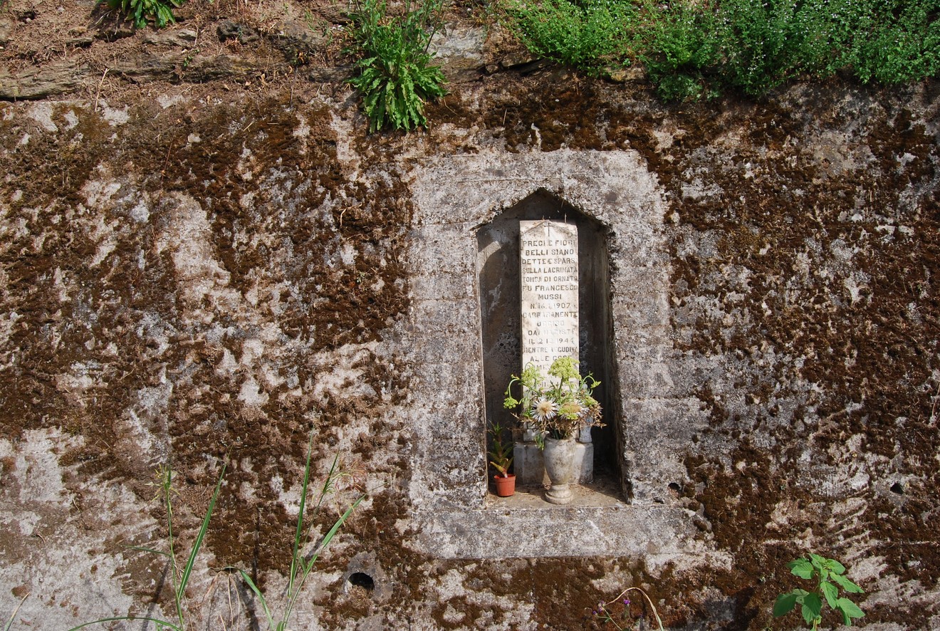 Cippo a Mussi incastonato nella roccia, con decorazioni vegetali e un vaso al suo interno.