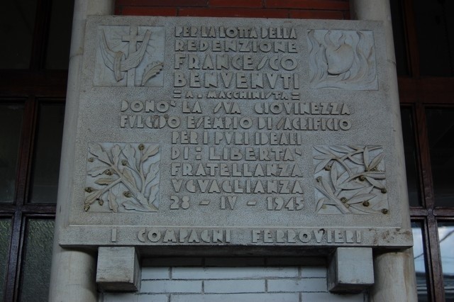 Lapide commemorativa dedicata a Francesco Benvenuti, con decorazioni in rilievo e un messaggio di ricordo.