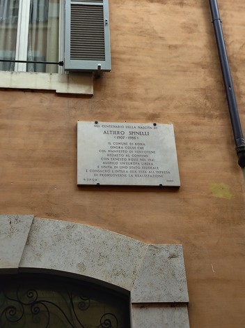 Lapide commemorativa a Spinelli, incastonata in una parete, con iscrizioni storiche e artistiche significative.