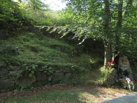 Fossa comune immersa nella vegetazione, con lastre in pietra e decorazioni floreali in memoria delle vittime.
