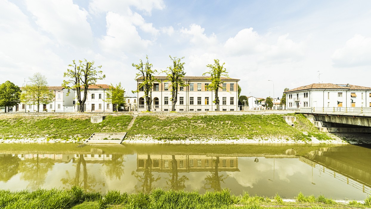 Monumento ai caduti della Resistenza, affacciato su un fiume, circondato da vegetazione e edificio storico.
