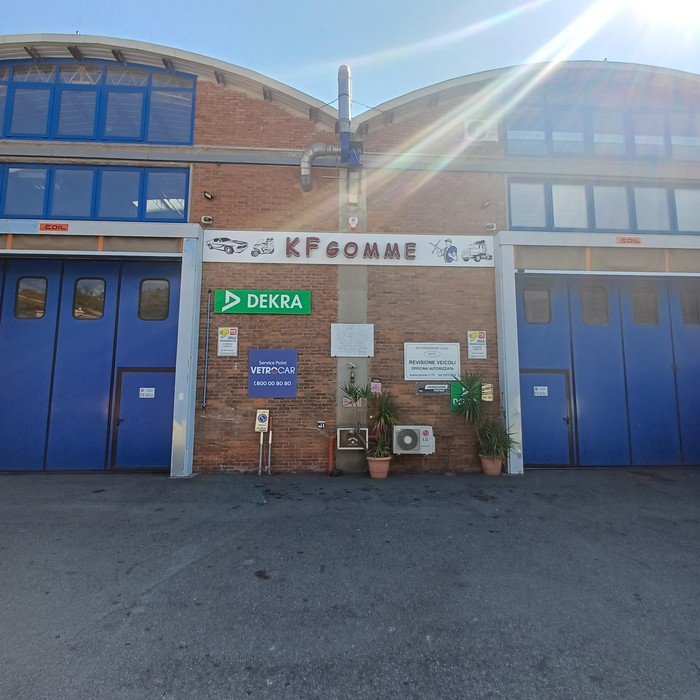 Facciata di un capannone industriale con insegna "KF Gomme", piccola targa con iscrizione tra le porte blu.