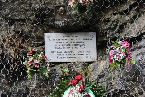 Lapide commemorativa dedicata a Biava, Chiesa e Ferrari, decorata con fiori e incastonata nella roccia.