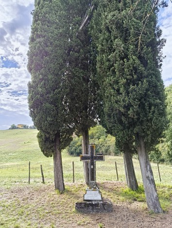 Croce a Bencini, circondata da cipressi in un paesaggio verdeggiante, simbolo di memoria e tranquillità.