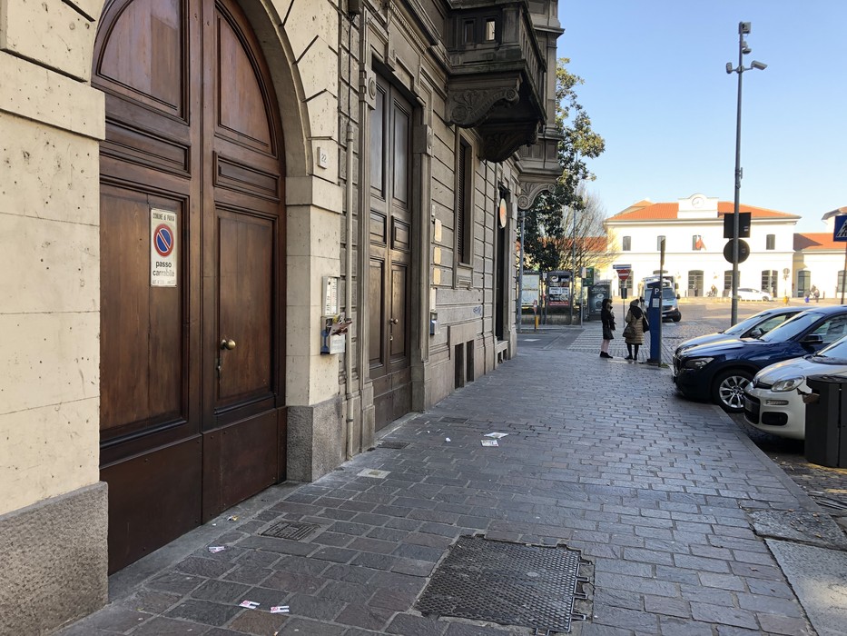 Pavimentazione urbana con pietra d'inciampo visibile e architettura storica sullo sfondo.