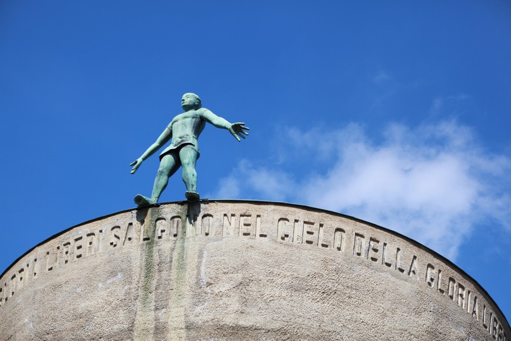 Monumento Ossario dei caduti partigiani con figura scultorea su un basamento, cielo azzurro sullo sfondo.