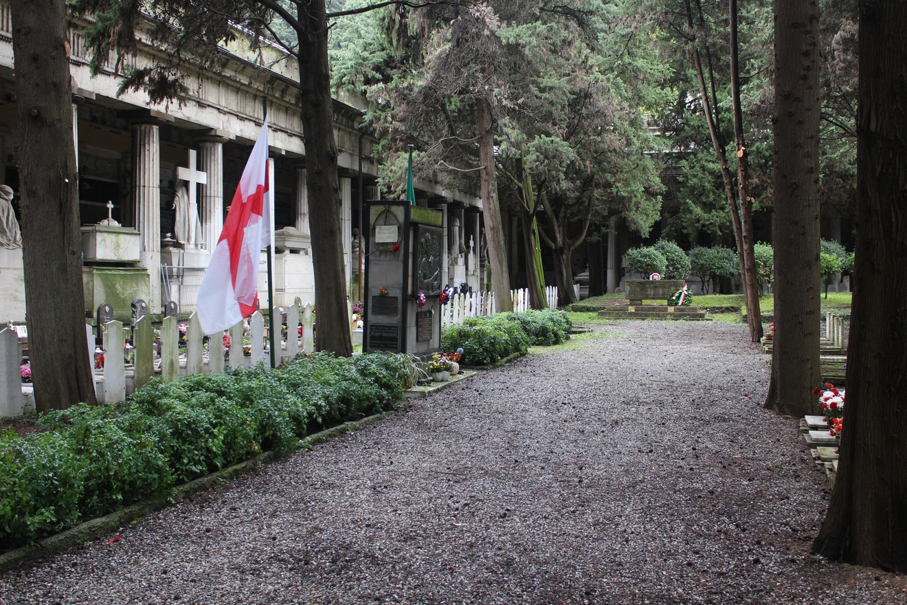 Il sepolcro di Poletaev in un cimitero, con bandiera e sentiero circondato da alberi e tombe.