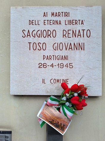 Lapide commemorativa in onore di Saggioro Renato e Toso Giovanni, con fiori e ornamenti tricolori.