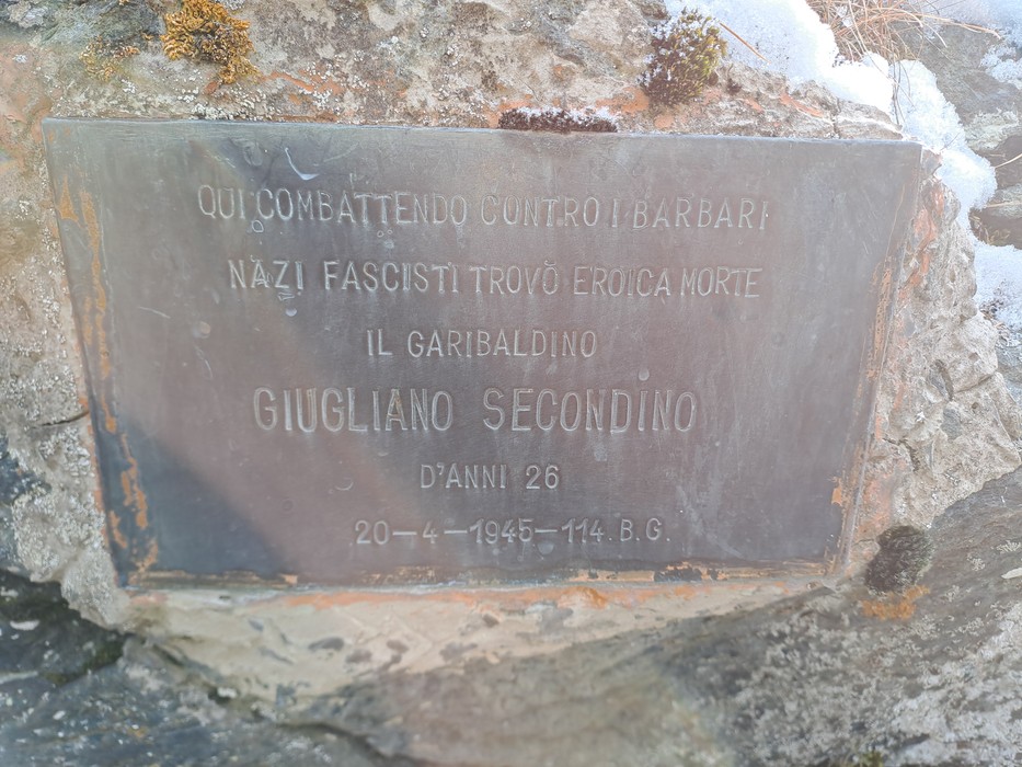 Targa bronzea con iscrizione fissata su una roccia, ai margini della foto tracce di muschio e neve.